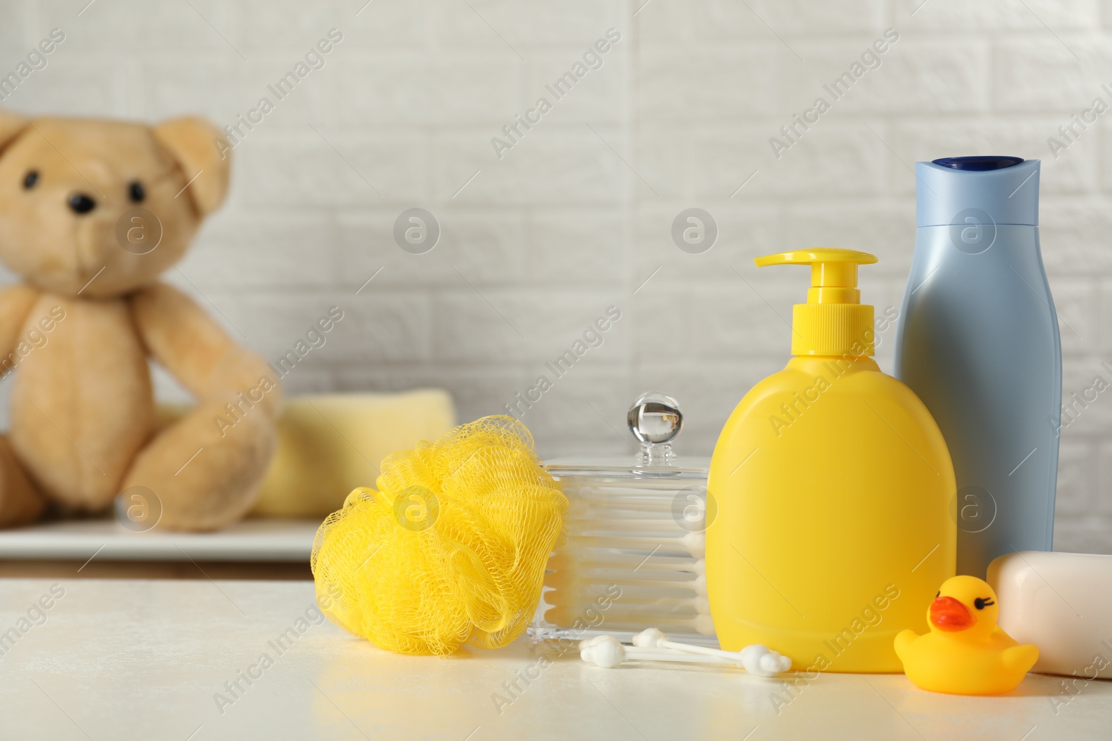 Photo of Baby cosmetic products, bath duck, sponge and cotton swabs on white table against brick wall