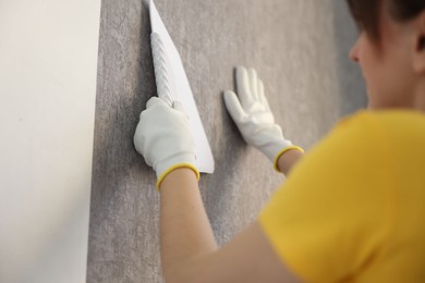 Photo of Woman smoothing stylish gray wallpaper in room, closeup