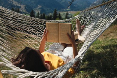 Photo of Young woman reading book in hammock outdoors on sunny day