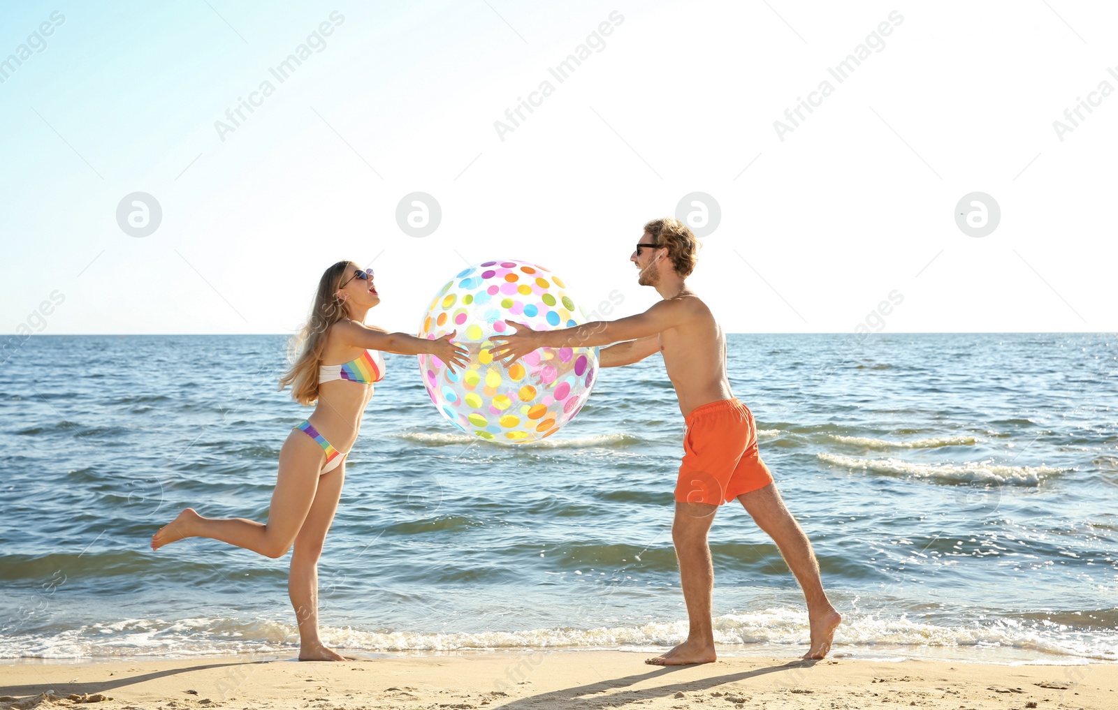 Photo of Happy young couple in beachwear playing with inflatable ball on seashore
