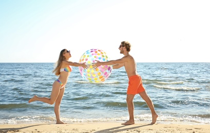 Happy young couple in beachwear playing with inflatable ball on seashore