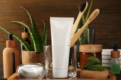 Aloe vera toothpaste in blank tube, brushes, green leaves and care products on table, space for text