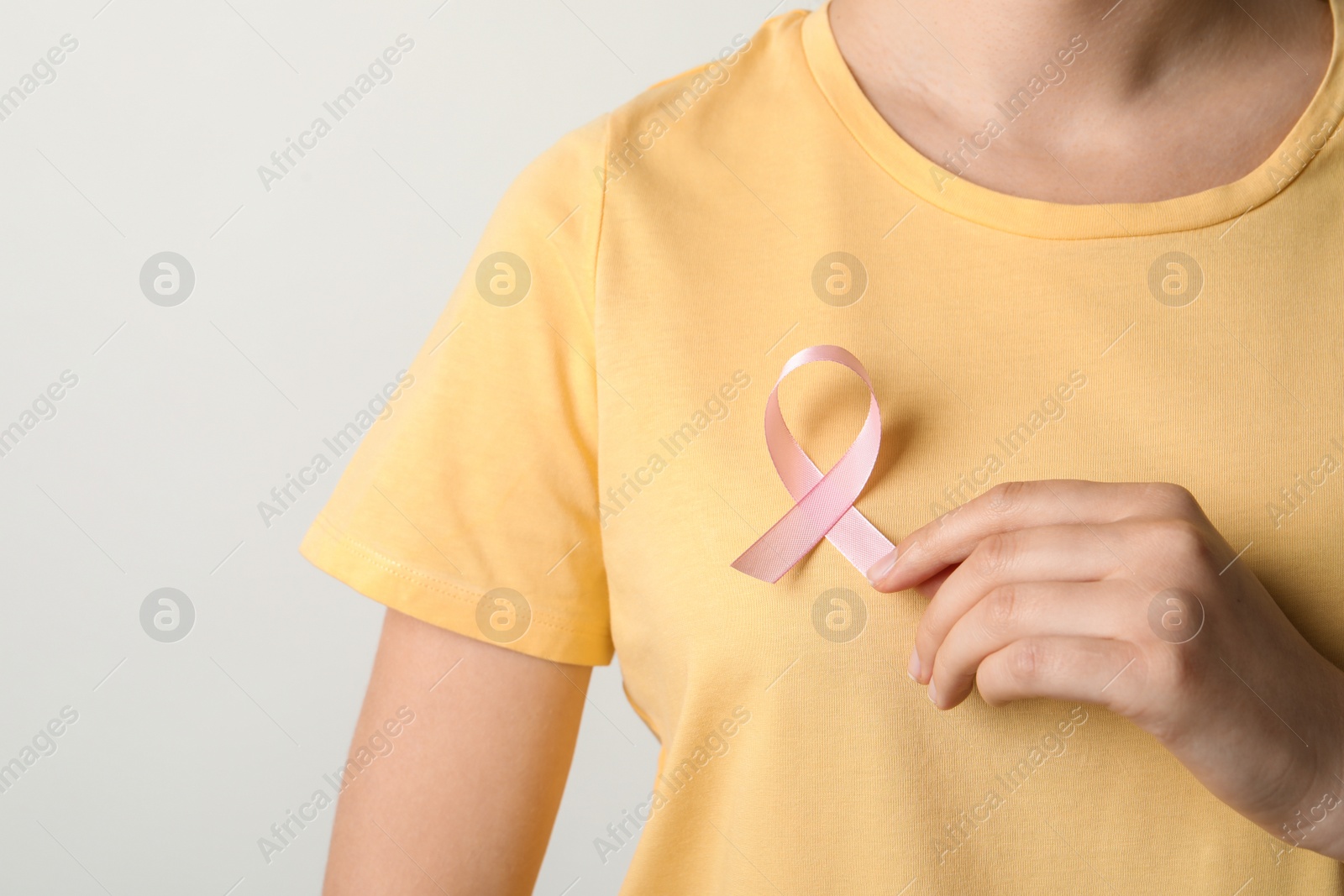 Photo of Woman with pink ribbon on t-shirt against light background. Cancer awareness