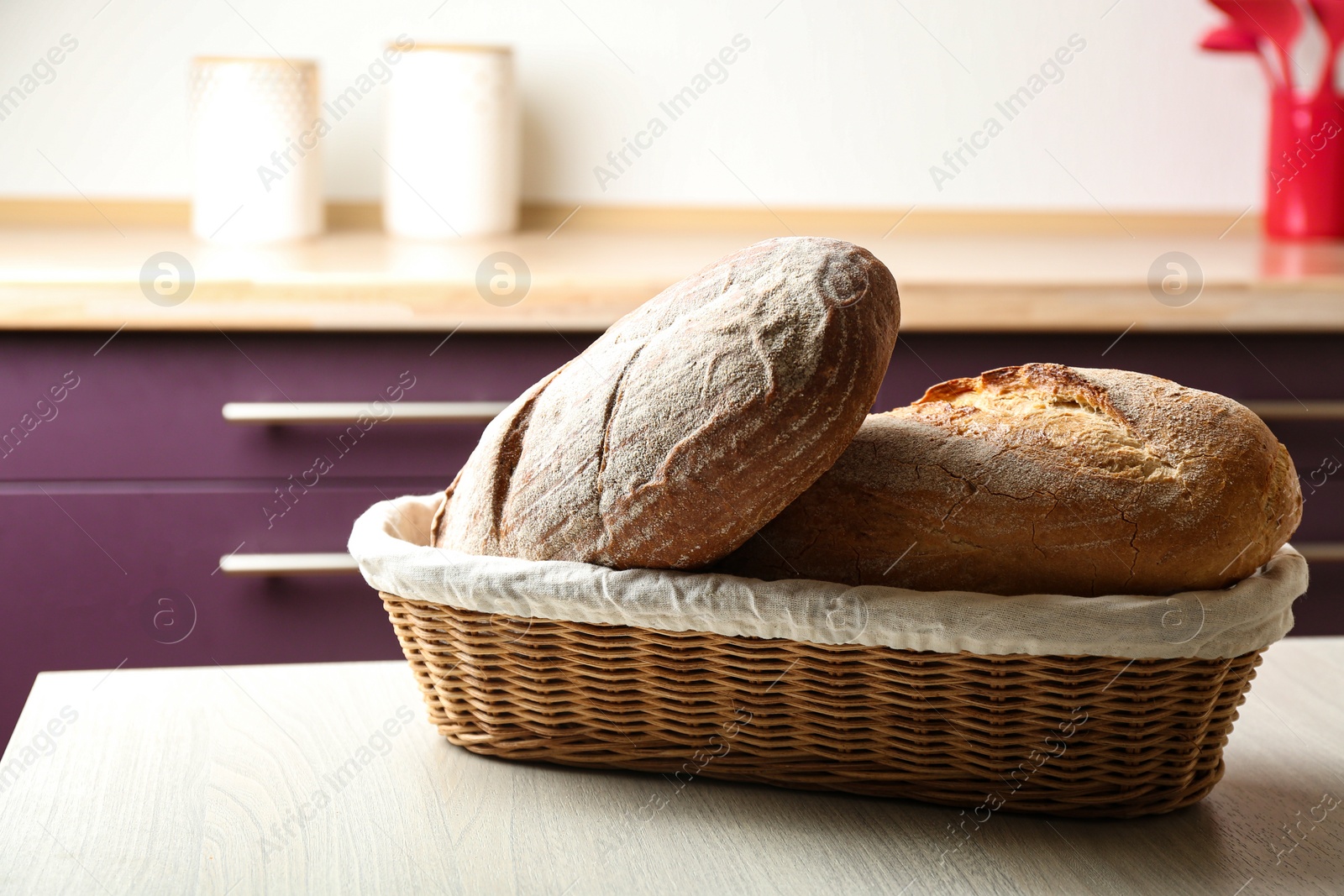 Photo of Wicker basket with loaves of tasty fresh bread on wooden table in kitchen