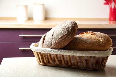 Photo of Wicker basket with loaves of tasty fresh bread on wooden table in kitchen