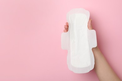 Photo of Woman holding sanitary napkin on pink background, closeup. Space for text