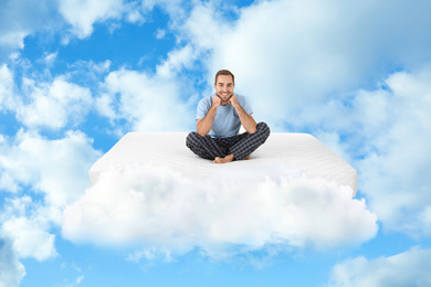 Young man sitting on mattress in clouds