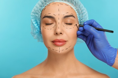 Photo of Doctor with pencil preparing patient for cosmetic surgery operation on light blue background, closeup