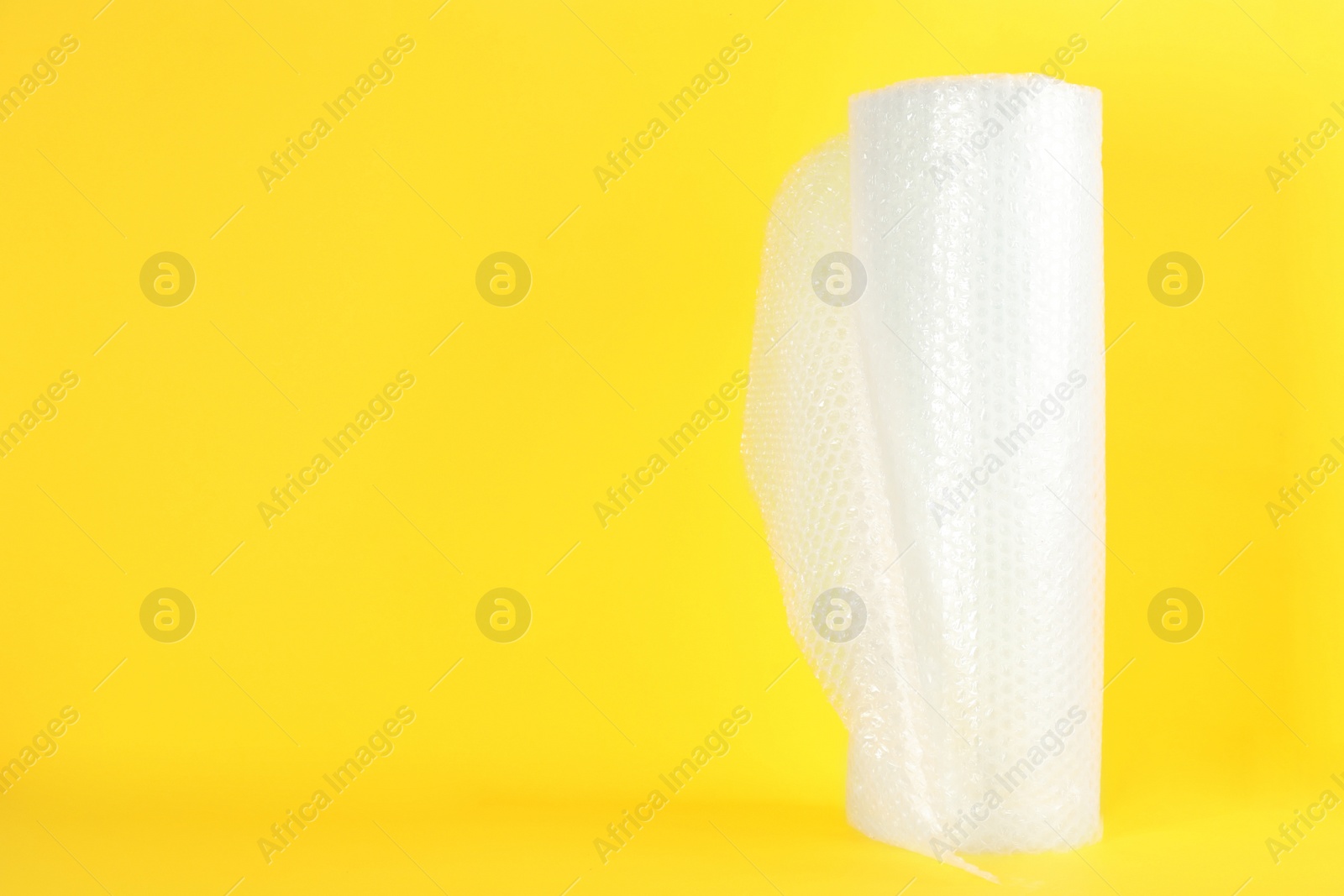 Photo of Bubble wrap roll on yellow background, space for text