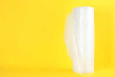 Photo of Bubble wrap roll on yellow background, space for text