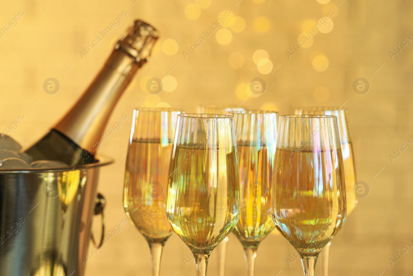 Photo of Glasses of champagne and ice bucket with bottle on blurred background