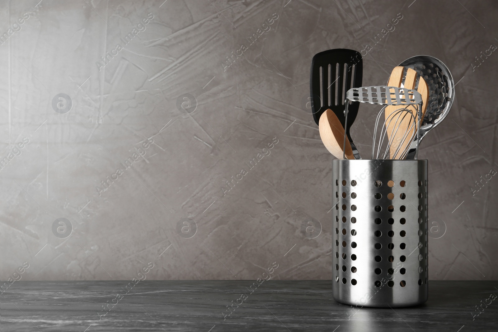 Photo of Holder with kitchen utensils on grey table against grey stone background. Space for text