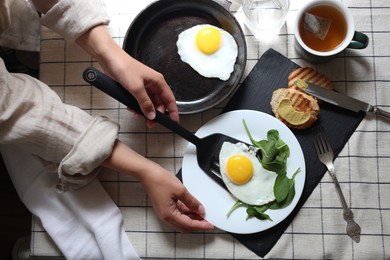 Woman putting tasty fried eggs onto plate at table, top view