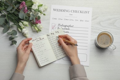 Photo of Woman writing in Wedding Planner at white wooden table, top view