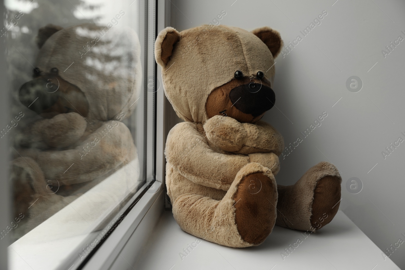 Photo of Cute lonely teddy bear on windowsill indoors. Space for text