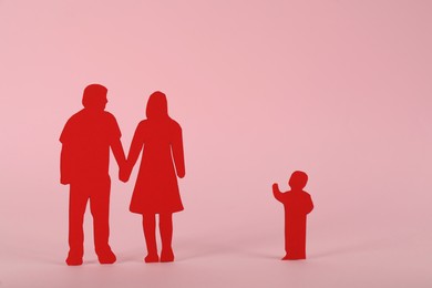Photo of Paper figures of couple and lonely kid on pink background. Child adoption concept