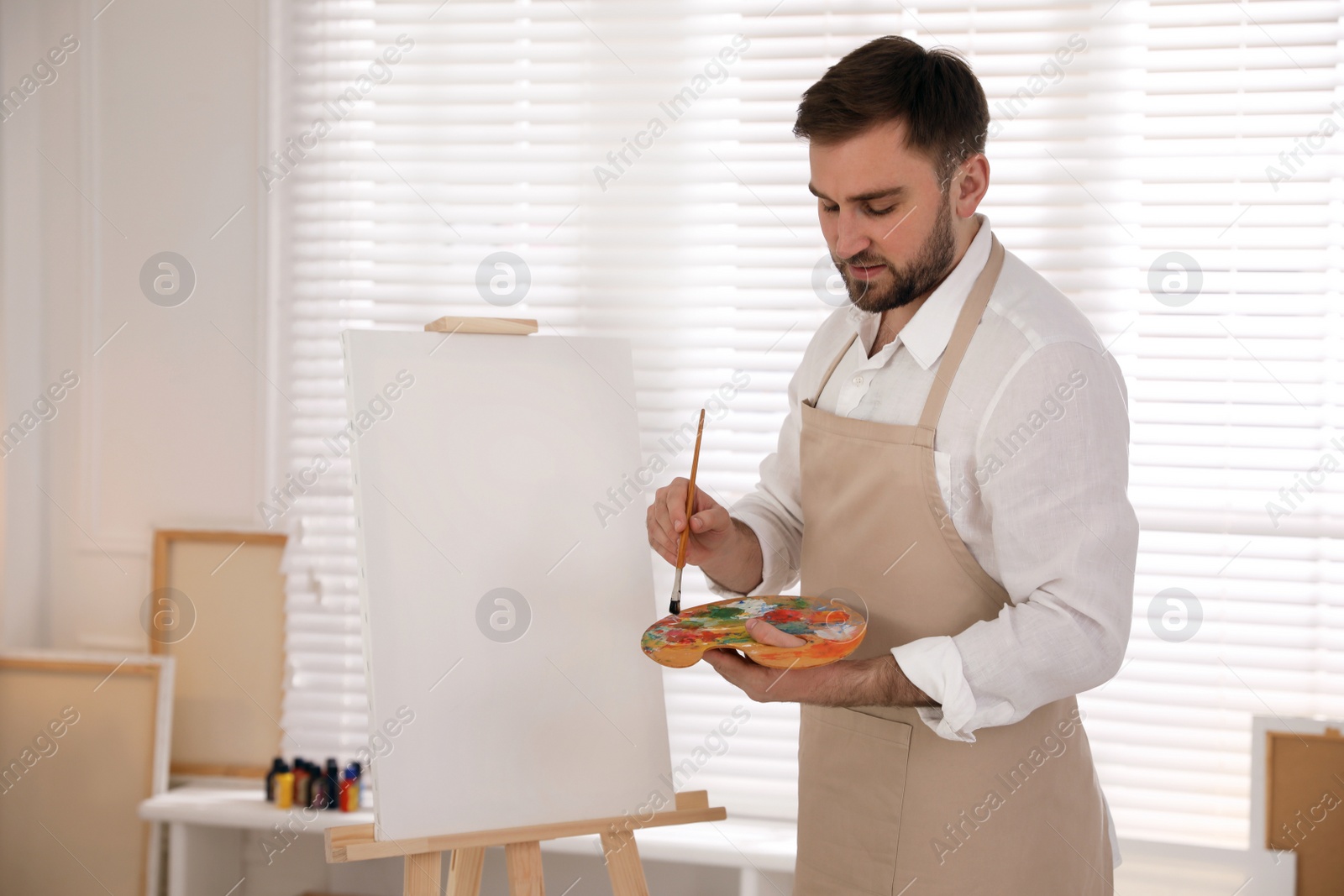 Photo of Young man painting on easel with brush in artist studio