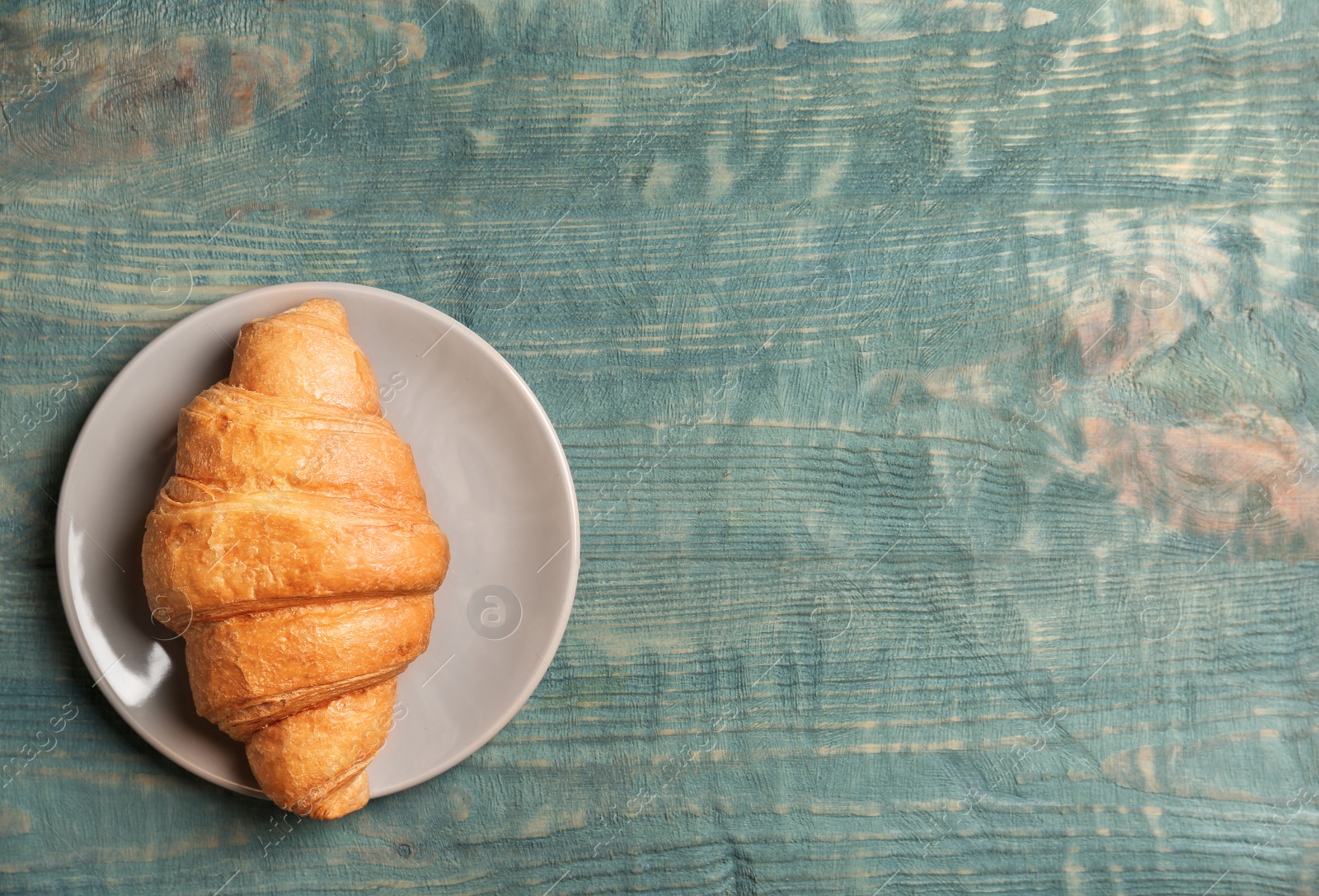 Photo of Plate with tasty croissant on wooden background, top view