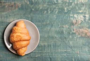 Plate with tasty croissant on wooden background, top view