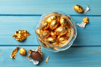 Chocolate eggs wrapped in golden foil on light blue wooden table, flat lay