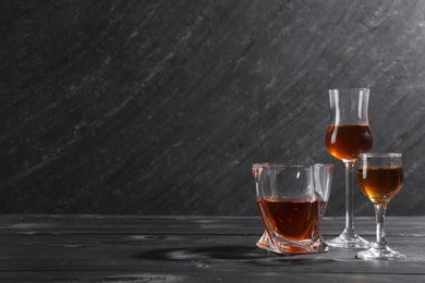 Different delicious liqueurs in glasses on black wooden table, space for text