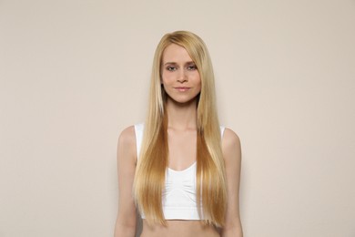 Beautiful young woman with long straight hair on beige background