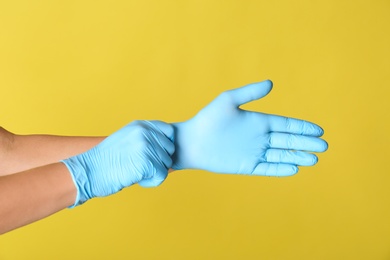 Person putting on blue latex gloves against yellow background, closeup