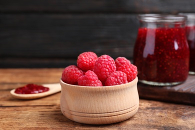 Fresh raspberries in bowl and jam on wooden table, closeup
