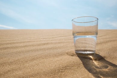 Glass of water on sand in desert. Space for text