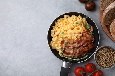 Photo of Delicious scrambled eggs with bacon in frying pan and ingredients on grey table, flat lay. Space for text