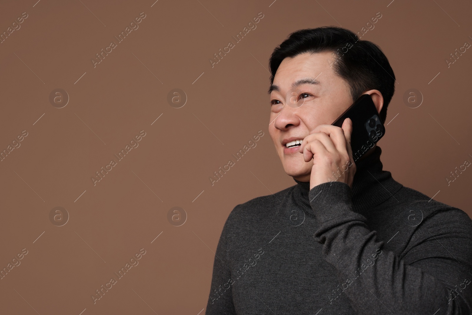 Photo of Portrait of happy man with smartphone on brown background. Space for text