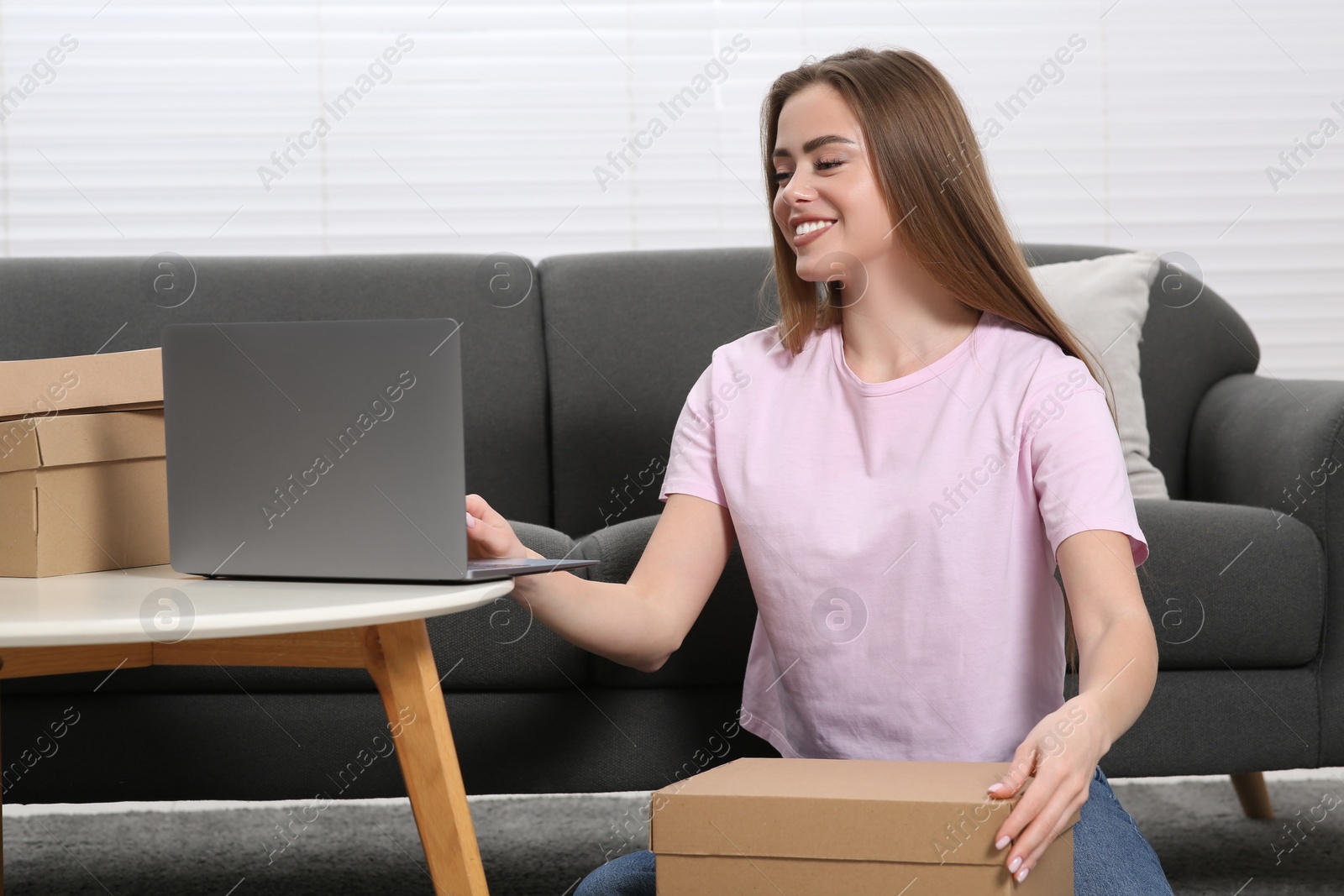 Photo of Happy woman using laptop while unpacking parcel at home. Online store