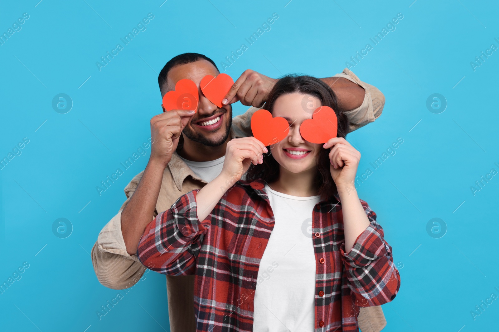 Photo of Lovely couple with red paper hearts on light blue background. Valentine's day celebration