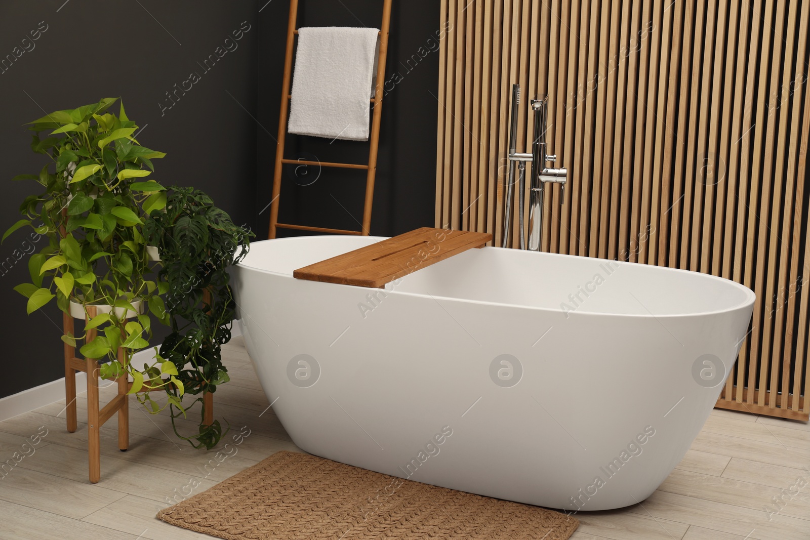 Photo of Spa day. Stylish bathroom interior with ceramic tub and green houseplants