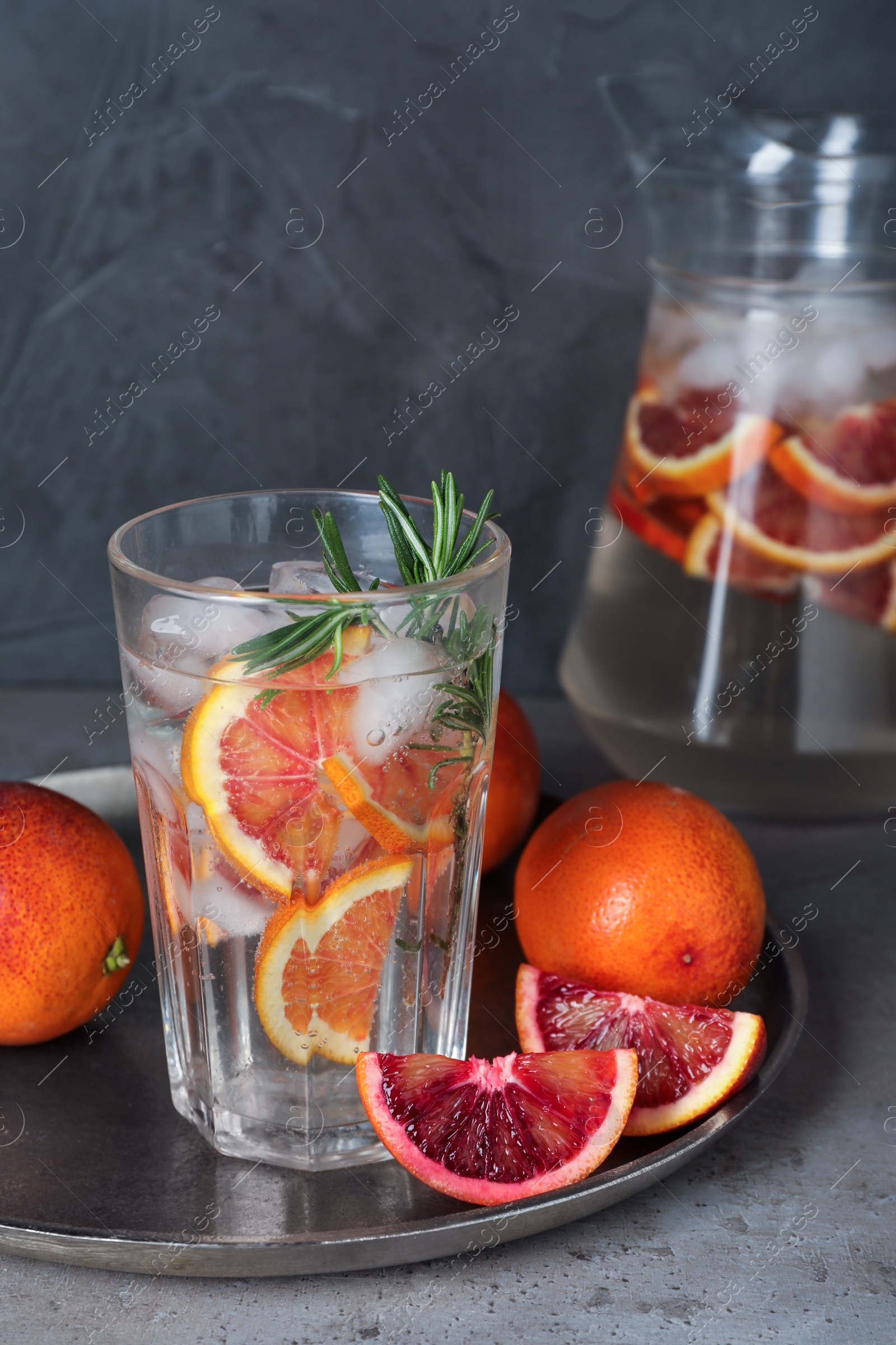 Photo of Delicious refreshing drink with sicilian orange and rosemary near fresh ingredients on grey table