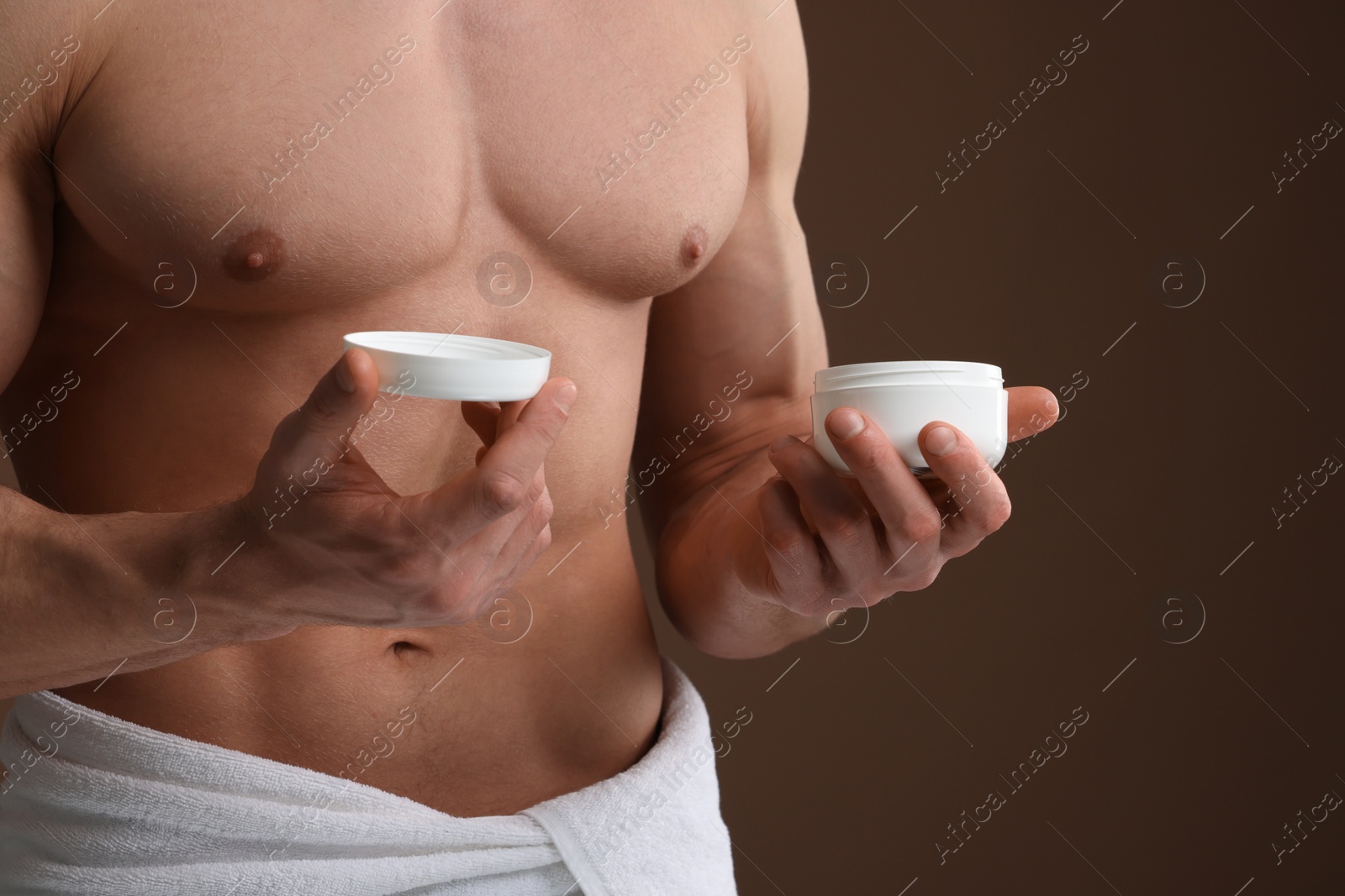 Photo of Handsome man holding jar with moisturizing cream on brown background, closeup