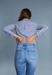 Woman suffering from back pain on grey background