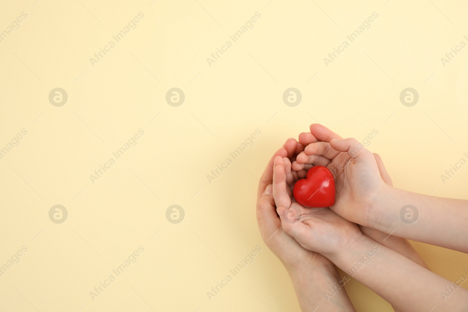 Photo of Mother with her child holding red heart on yellow background, top view. Space for text