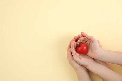 Photo of Mother with her child holding red heart on yellow background, top view. Space for text