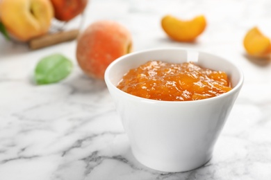 Photo of Bowl with tasty peach jam on marble table