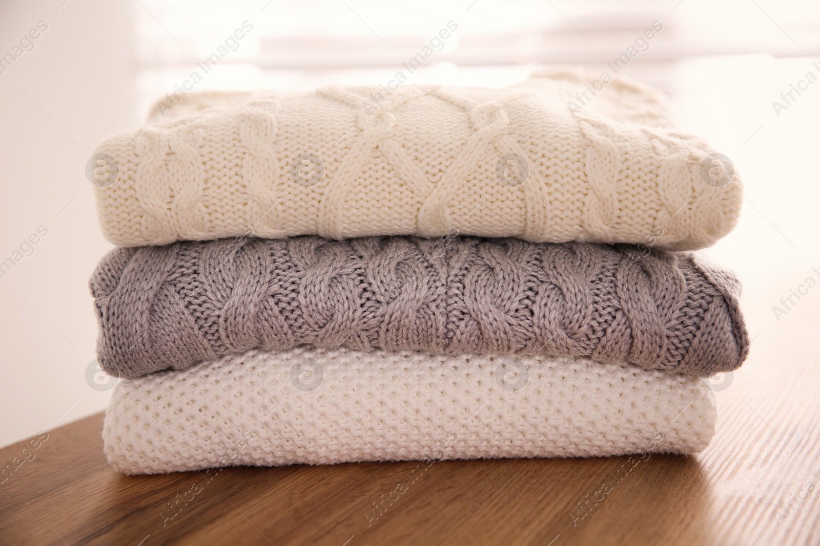 Photo of Stack of folded warm sweaters on wooden table indoors, closeup