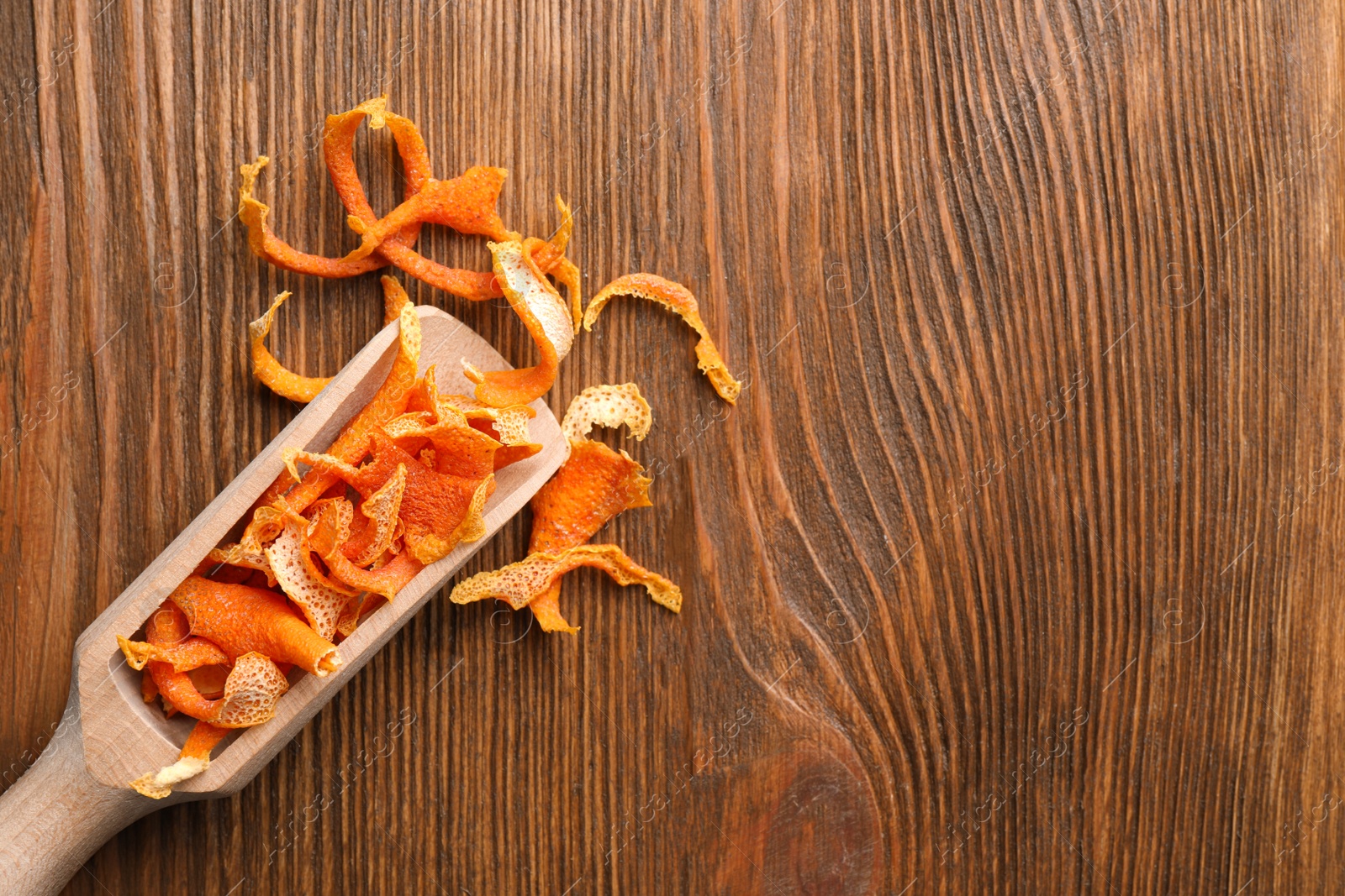 Photo of Scoop with dry orange peels on wooden table, flat lay. Space for text