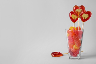 Glass with different candies on light background, space for text