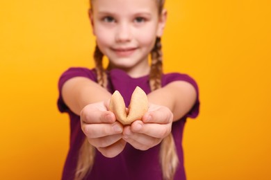 Photo of Cute girl holding tasty fortune cookie with prediction on orange background, selective focus