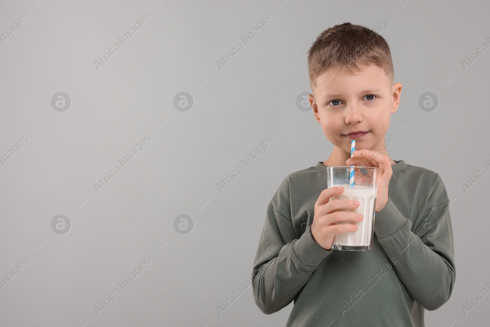 Photo of Cute boy with glass of fresh milk on light grey background, space for text