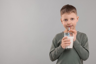 Photo of Cute boy with glass of fresh milk on light grey background, space for text