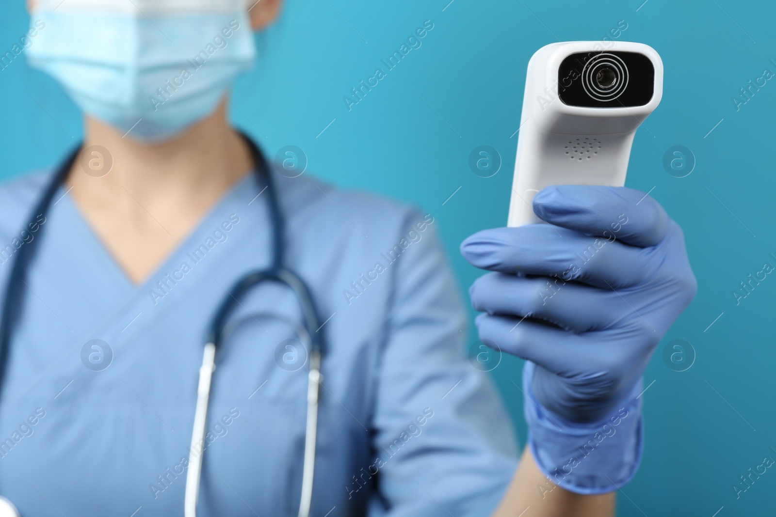 Photo of Doctor with infrared thermometer on blue background, closeup. Checking temperature during Covid-19 pandemic