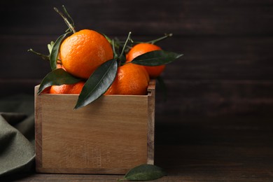 Photo of Crate with fresh ripe tangerines and leaves on wooden table. Space for text