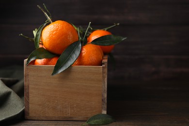 Crate with fresh ripe tangerines and leaves on wooden table. Space for text