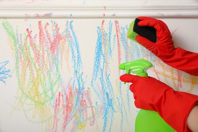 Photo of Woman erasing child's drawing from white wall, closeup